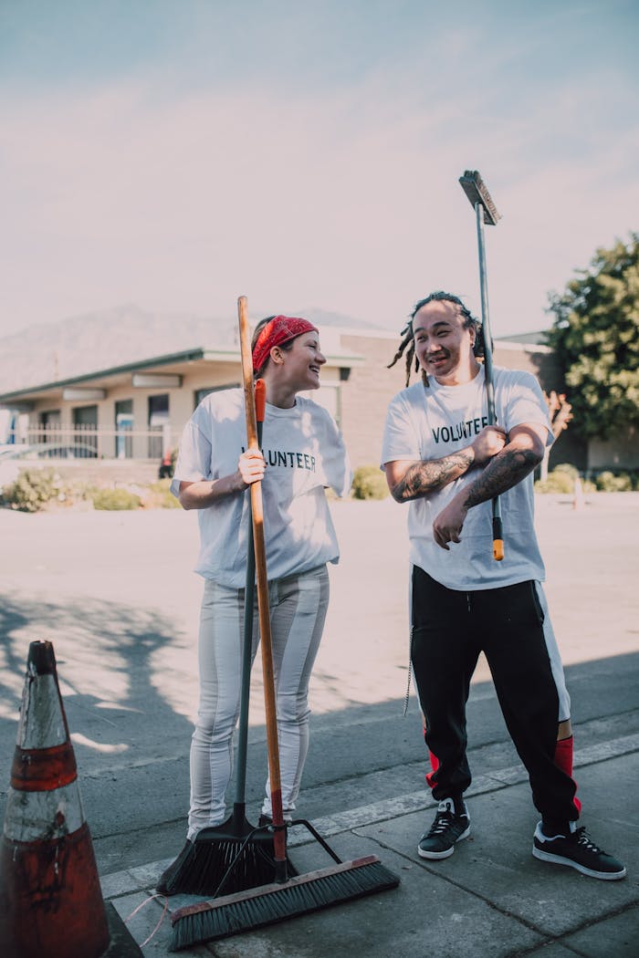 Two volunteers clean the street with brooms, fostering community spirit and social good.