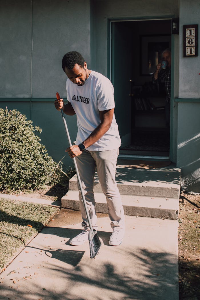 A man in a volunteer shirt sweeping outdoors, showcasing community service.